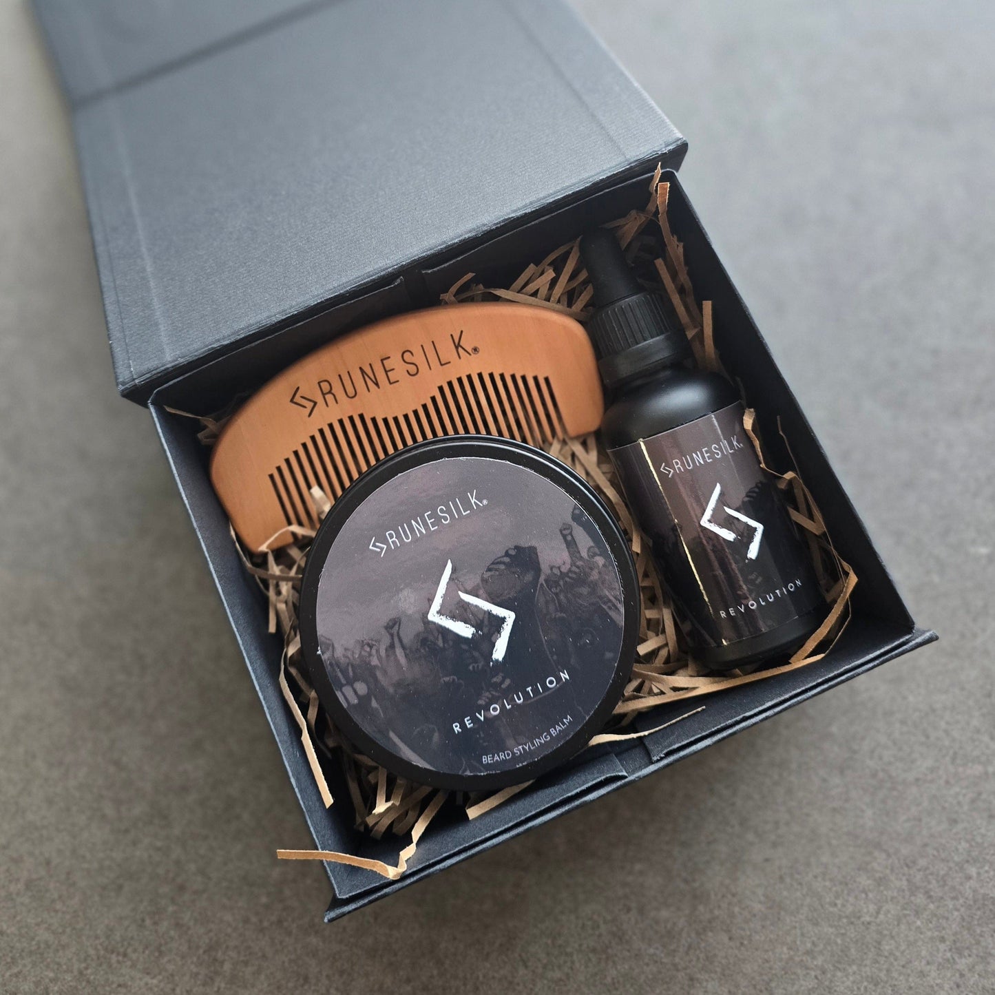 Brunesilk grooming products including a comb, tin and bottle in a box on a gray background